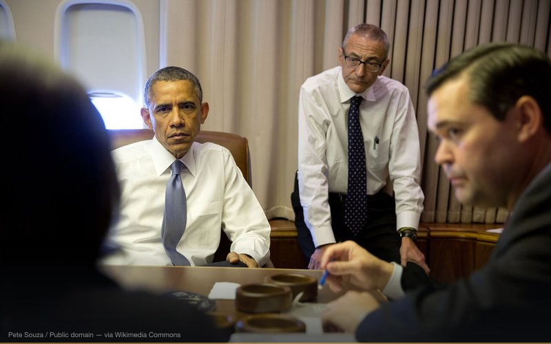President Barack Obama holds a meeting with National Security Advisor Susan E. Rice; John Podesta, Counselor to the President; and Phil Reiner, Senior Director for South Asian Affairs, aboard Air Force One en route to New Delhi, India. — related to Pizzagate Conspiracy Theory